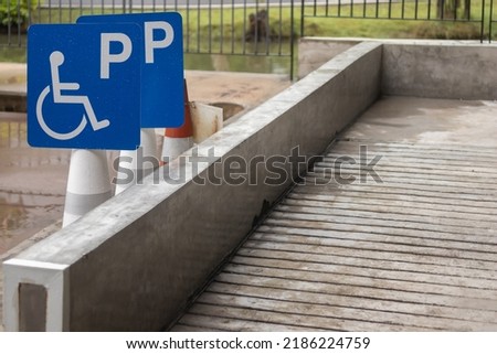 Blue wheelchair sign or handicapped parking symbol stick on white traffic cone with blurred outdoor disable ramp background.
