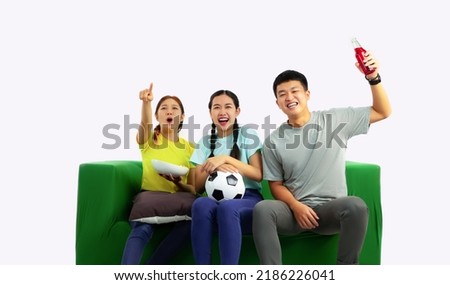 Young asian man and women holding football ball sitting on green sofa and cheering the soccer game at home on the white screen background.