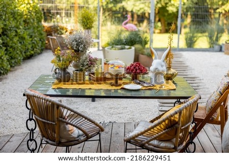Beautiful and cozy dining place on wooden terrace at backyard. Cheese cake on garden table decorated with flowers