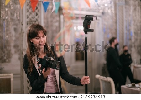 Girl photographer with a camera at work on the set in the banquet hall. A young beautiful woman - a professional photographer with a camera and a flash takes pictures on a holiday in a decorated hall