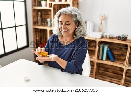 Middle age grey-haired woman taking pills sitting on the table at home. Royalty-Free Stock Photo #2186239955