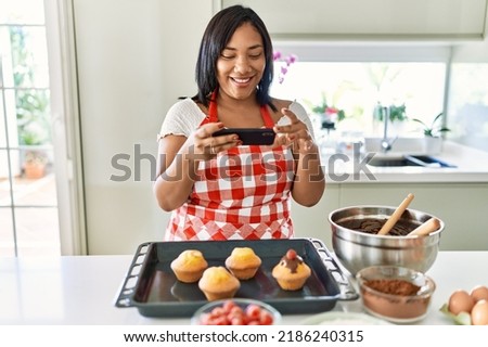 Hispanic brunette woman taking photo of chocolate muffins at the kitchen