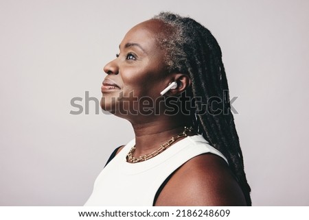 Mature woman with dreadlocks listening to some music on wireless earphones. Fashionable middle-aged woman enjoying her favourite playlist  against a studio background.