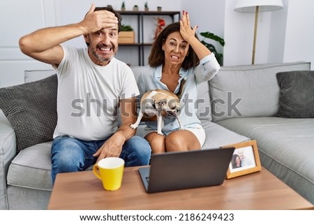Hispanic middle age couple sitting on the sofa using computer laptop stressed and frustrated with hand on head, surprised and angry face 
