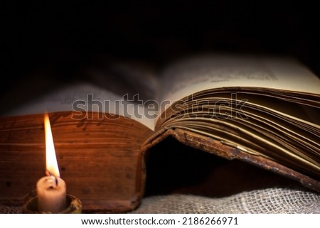 Opened old book on a dark background. Selective focus on the pages of the book. A photo with a shallow depth of field. In the foreground is a defocused image of a candle.