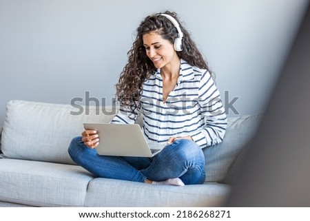 A young female student sitting on the desk, using headphones when studying. Copy space. Photo of a young woman sitting on the sofa in the living room, using laptop and listening music