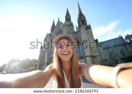 Smiling tourist girl takes self portrait in front of Salford Cathedral, Manchester, England