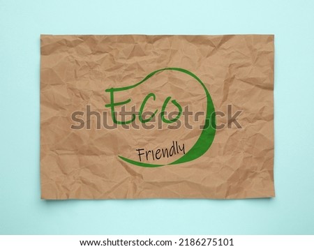 Sheet of crumpled paper with phrase Eco Friendly on light blue background, top view