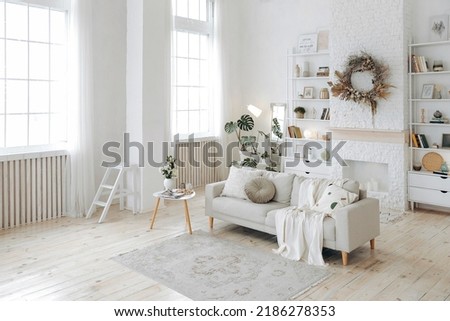 Modern stylish white living room with large windows and scandinavian style sofa against the backdrop of a fireplace and shelving and potted plants. Nobody Royalty-Free Stock Photo #2186278353