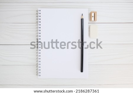 Notepad on a metal spiral, black pencil, sharpener and eraser on a wooden table. Minimalistic concept of sketch drawing, learning to draw. Top view, space for text.