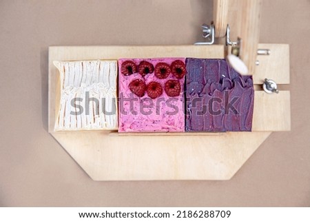 Multi-colored handmade soap in a special wooden device for cutting it into pieces. White, pink and purple soap with berries. Top view