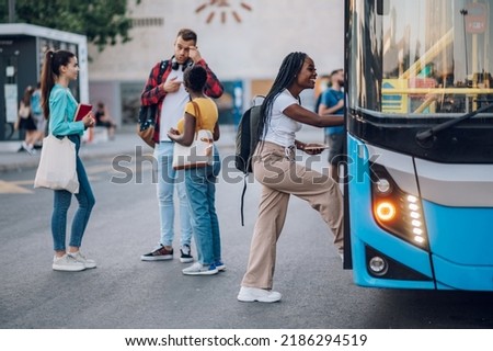 Multiracial passengers waiting at a bus stop and talking cheerfully. Focus on an african american woman entering the bus. Diverse tourists in new town. Best friends traveling together in a city. Royalty-Free Stock Photo #2186294519