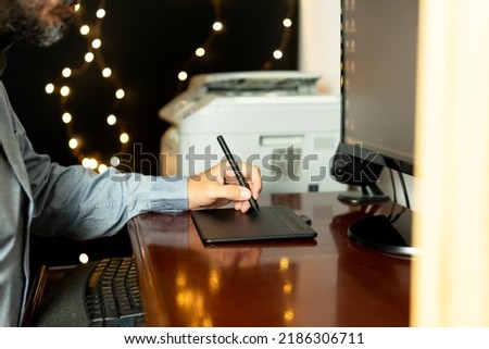 Young left-handed graphic designer sitting at his workspace using digital graphic tablet. Working professional. Freelance.