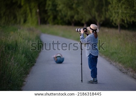 Child holding professional camera with lens standing on monopod on the road in rural area europe, summer photoshooting girl taking photo of the countryside