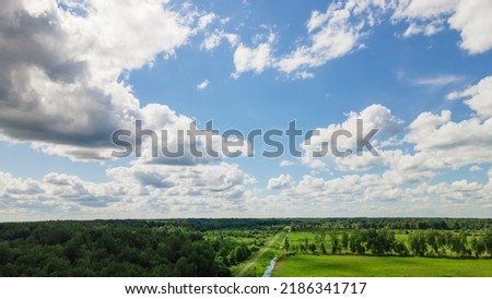 Blue sky panorama with clouds over tops of green trees. Blue sky and white cloud soft. White clouds background. Green tree top line over blue sky and clouds background in summer.