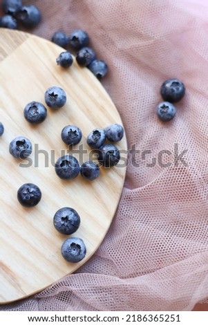 Berries of juicy blue sweet wild blueberries lie on a wooden kitchen round stand on a pink airy fabric. for prints advertising flower shops flyers banners labels and screensavers