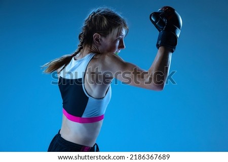 Defense stance. Sportive teen-girl, MMA fighter in action, motion isolated on blue background in neon light. Concept of sport, competition, action, achievements. Copy space for ad. Royalty-Free Stock Photo #2186367689