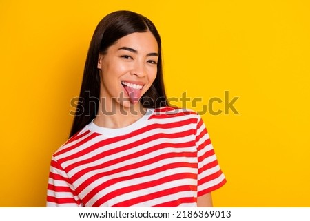 Photo of pretty overjoyed girl toothy smile show tongue out wear red white stripes t-shirt isolated on yellow color background