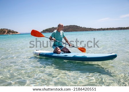 Sup surfing. Beautiful view of the sea with a mature man kneeling on a board with paddle in the water. Standup paddleboarding in summer