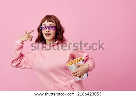 Excited overjoyed happy cute redhead lady in pink hoodie sunglasses with popcorn posing isolated on over pink studio background show copy space Banner. Fashion Cinema concept. Entertainment offer