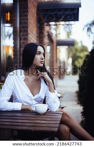 Pretty trendy girl drinking coffee in street cafe. Portrait of brunette young model woman.  Royalty-Free Stock Photo #2186427743