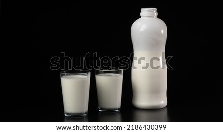 Glass with milk or kefir on a black background with a white bottle