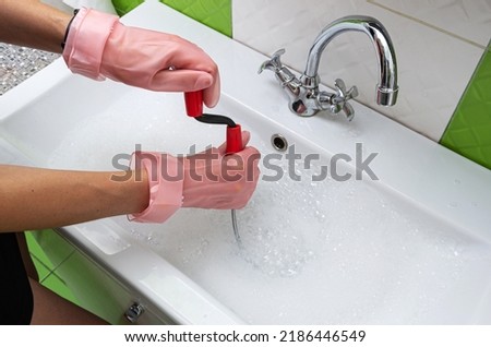 Woman in protective rubber gloves unblocking  a clogged sink with a probe or drained cable at home.  Royalty-Free Stock Photo #2186446549