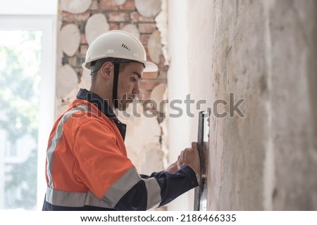 A worker in a helmet makes repairs in the apartment,finishing work. A man is engaged in interior decoration of the building, wall putty Royalty-Free Stock Photo #2186466335