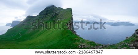 Panoramic view on road going to the village of Trollanes located on the island of Kalsoy in Faroe Islands with mountains of Kunoy and Bordoy in the background.