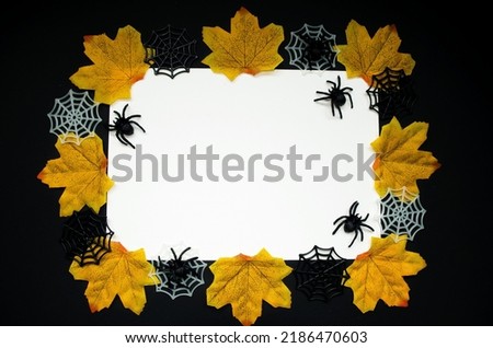 On a black background, an invitation card for the Halloween holiday, a white sheet of paper with copy space for text, autumn leaves, cobwebs and spiders.  Close-up, frame.