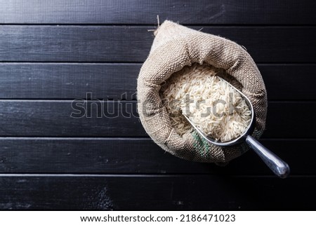 Uncooked white rice in a burlap sack on black table. Top view.