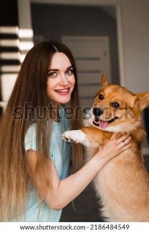 Domestic Corgi dog with girl owner. Young woman sitting on the floor and hug Welsh Corgi Pembroke. Lifestyle with domestic playful dog