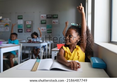 African american elementary school students with hands raised sitting at desk in classroom. unaltered, education, childhood, learning and school concept. Royalty-Free Stock Photo #2186487749