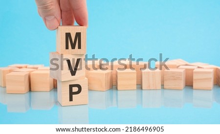 hand holding wood cube block with text MVP - Minimum Viable Product. the inscription on the cubes is reflected from the surface. blue background with copy space.