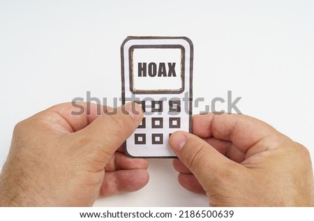 Technology and security concept. On a white background, in the hands of a person, a cardboard model of a telephone with an inscription on the screen - HOAX