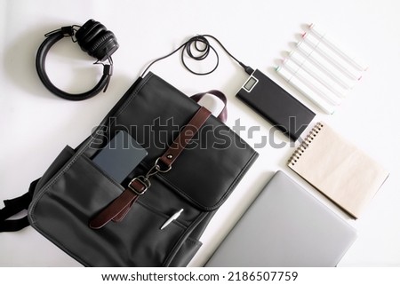 Modern urban backpack for laptop with smartphone and pen lies next to laptop, power bank, headphones, notepad and felt-tip pens - markers. Study, design and lifestyle with gadgets. Close-up Royalty-Free Stock Photo #2186507759
