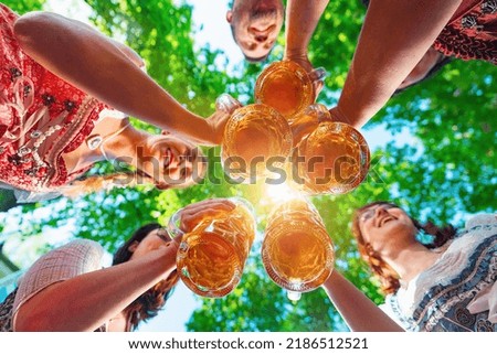 Toasting in Bavarian beer garden. Group of happy friends drinking and toasting beer in Bavarian traditional costume at  Oktoberfest, folk or beer festival, munich, germany Royalty-Free Stock Photo #2186512521