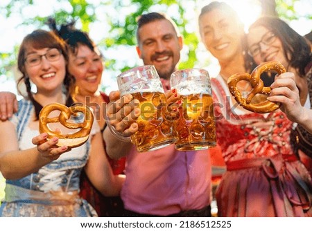 friends in Tracht, Dirndl and Lederhosen having fun drinking beer and eating pretzels in Beer garden or oktoberfest in Bavaria, Germany Royalty-Free Stock Photo #2186512525