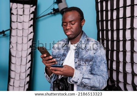 Young customer using debit card for online payment while standing in production studio with professional photo equipment. Man with DSLR camera paying cashless on digital retail store.