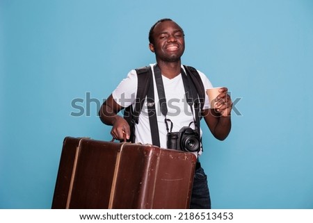 Happy photography enthusiast with luggage and DSLR camera getting ready for holiday journey departure. African american photographer having baggage, backpack and photo device ready for citybreak.