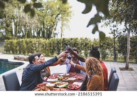 Multiracial group of friends having a celebratory toast during the birthday dining in the courtyard of the farmhouse by the pool - people lifestyle and weekend activities lifestyle concept