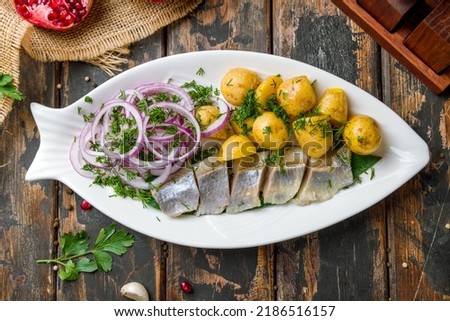 Sliced Herring with mini potatoes and red onion on white plate top view on old wooden table Royalty-Free Stock Photo #2186516157