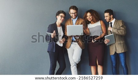 Diverse group of business people with technology browsing, searching and reading positive online reports, data or charts on laptop. Team of creative marketing agents against grey wall with copy