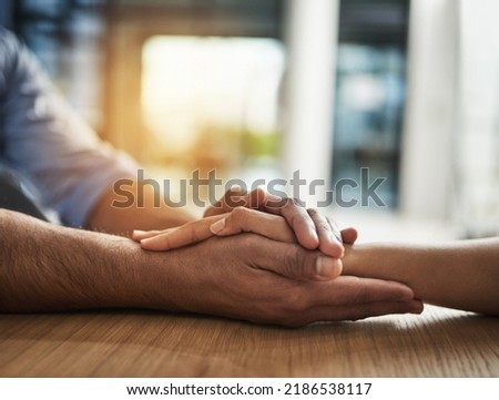 Kindness, support and trust between two people holding hands while sitting at a table together. Closeup of two people talking through hard time or discussing a problem while showing concern and love Royalty-Free Stock Photo #2186538117