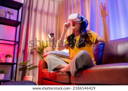 young attractive casual asian female woman watched the performance lives streaming concert in virtual reality through VR glasses goggle on sofa with fun and joyful moment in living room at home Royalty-Free Stock Photo #2186546429