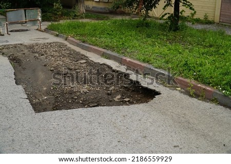 Large pit on the road with a fence and warning signs. Subsidence of soil. Collapse. A large pit on the road fenced