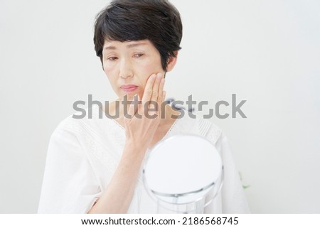 Asian senior woman looking in the mirror at home Royalty-Free Stock Photo #2186568745
