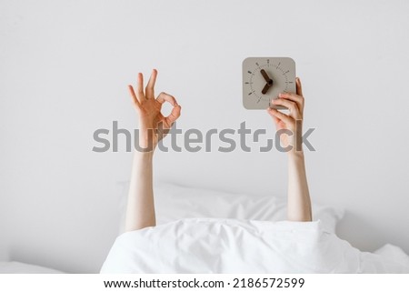 Person's hand holding compact clock after awakeness and showing OK sign, morning concept, people getting up early, time management, alarm clock, hotel room details