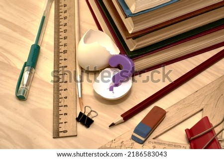 a stack of books writing materials stationery clips and a split chicken egg with the letter A inside on the table the concept of knowledge education school. High quality photo