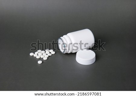 Unlabelled white plastic pill bottle. Poured out several small white pills. out side in black background Royalty-Free Stock Photo #2186597081